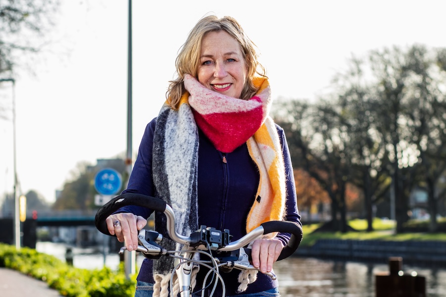 Ik rij graag in het zand. 9 Blonde vrouw met gekleurde sjaal op fietspad langs het water.