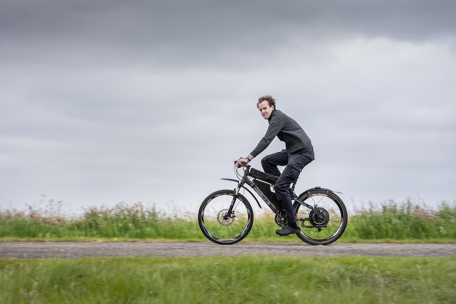 Man fietst op zwarte fiets met motor in het achterwiel over een landweg.