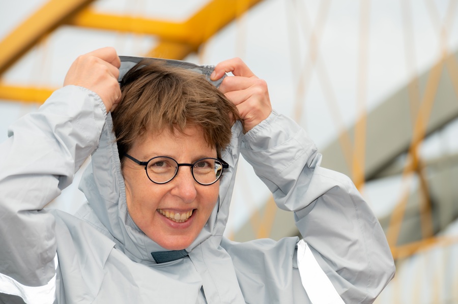 Lachende vrouw trekt lichtgrijze capuchon over haar hoofd.